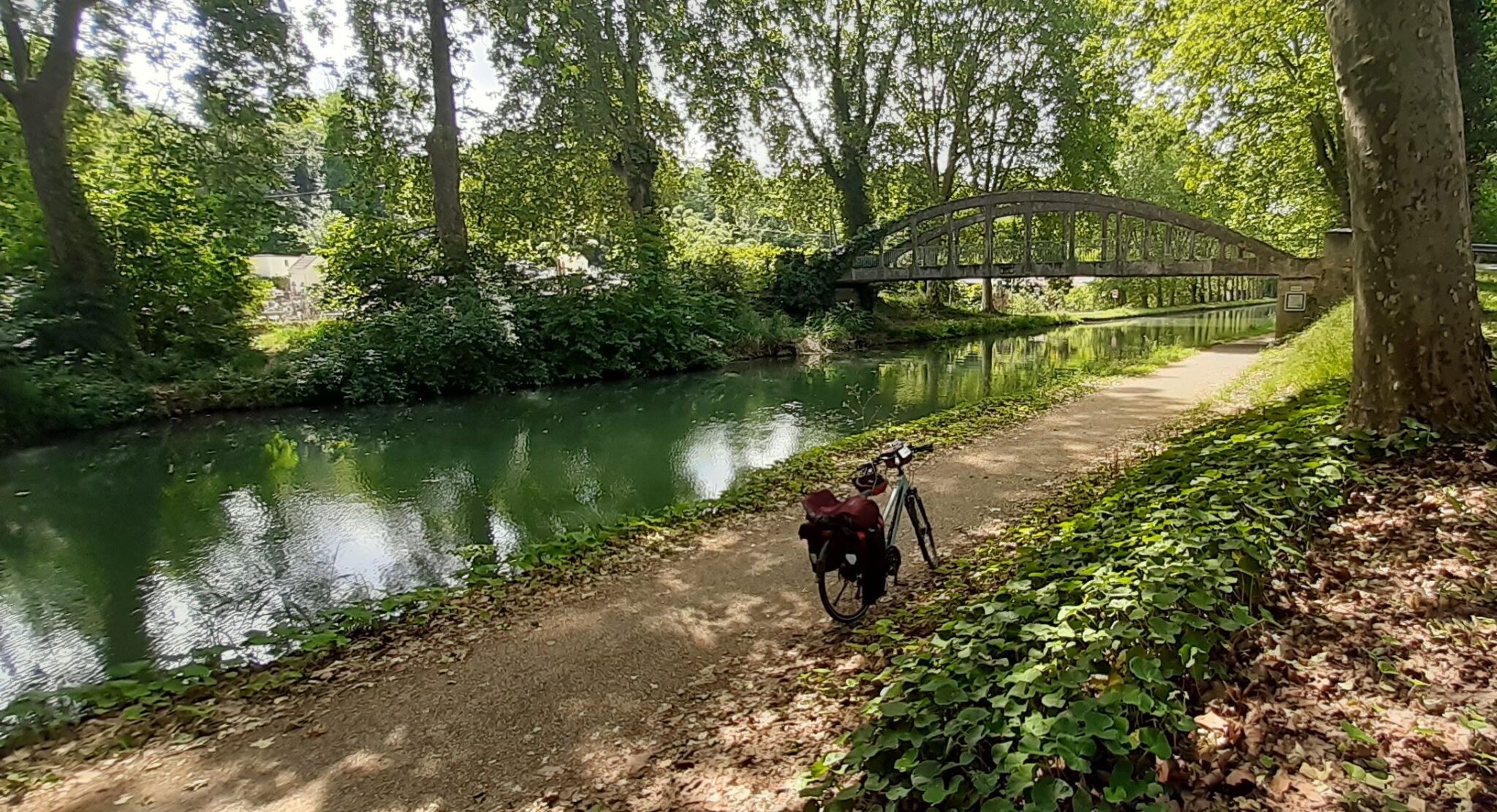 Canal de la garonne avec un pont et son eau verte, sa piste cyclable et un vélo.